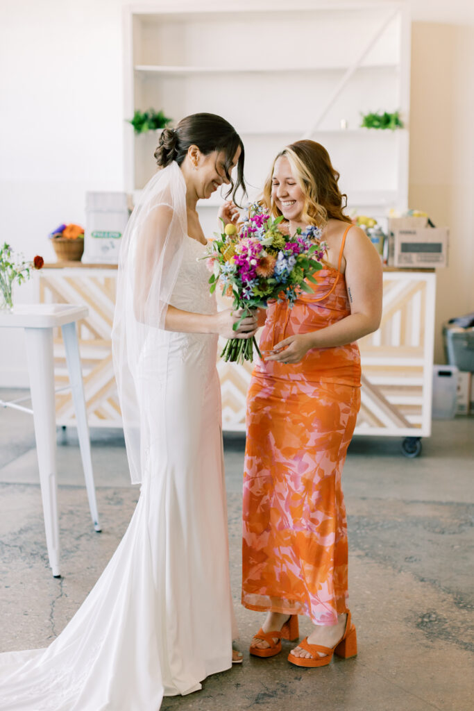 A bride laughs with a bridesmaid wearing a coral bold accent dress