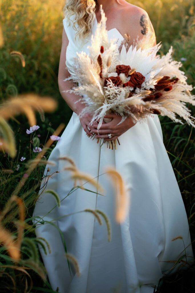 A bride holds a large bouquet of dried florals and long grasses at her nature inspired wedding