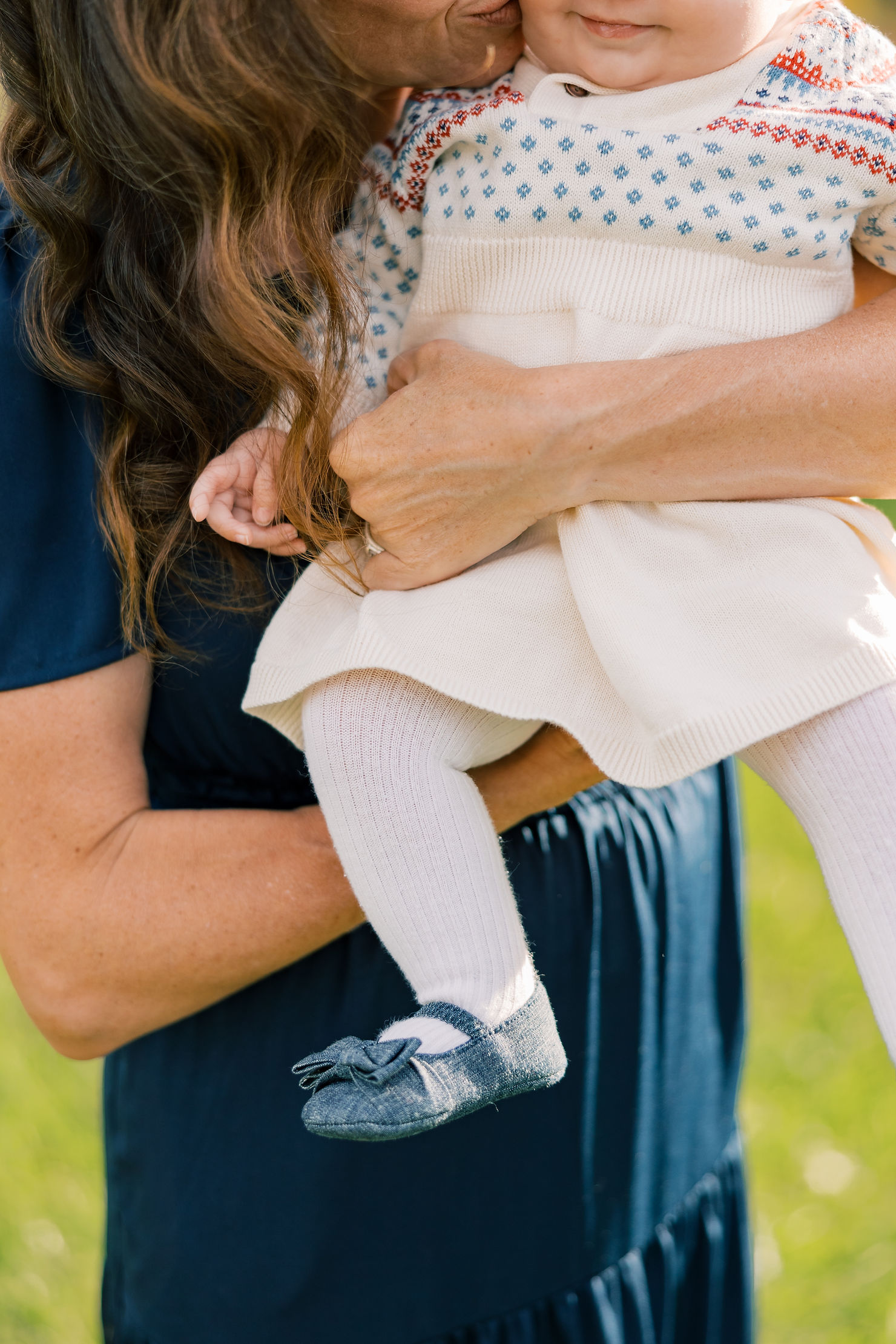 Close-up of a mother's hands holding her child's hands, with floral details in the background during a Mother's Day mini session.