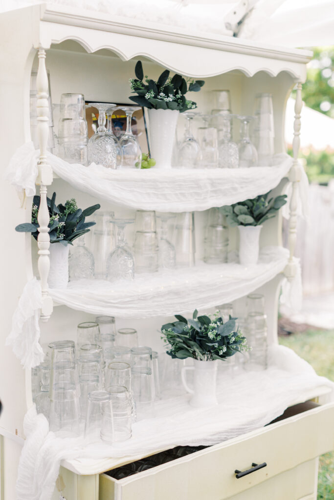 A china cabinet is repurposed for this backyard wedding to hold glasses for guests