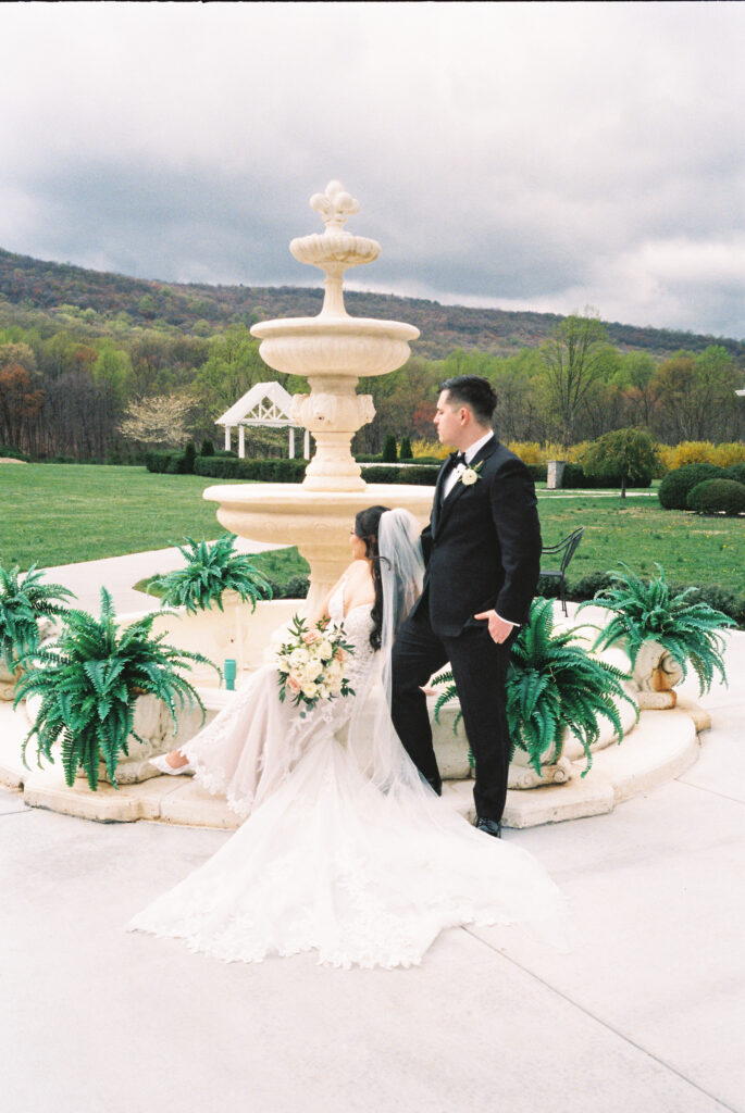 A couple stands in front of a fountain at their opulent wedding in Italy