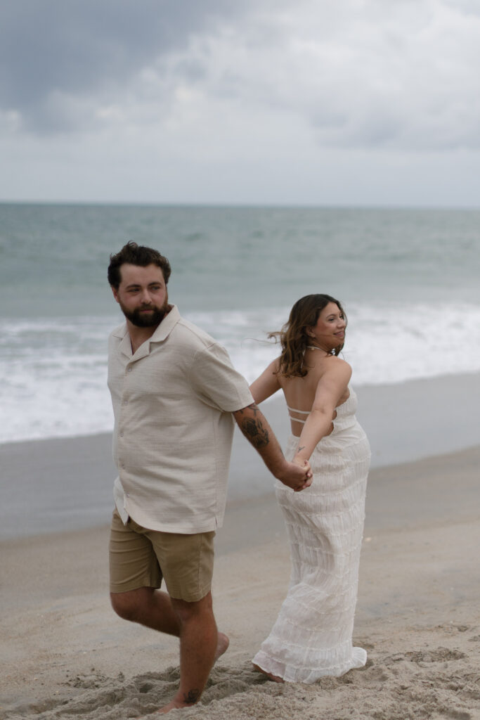 Couple twirling by the waves, movement captured against deep clouds rolling overhead.