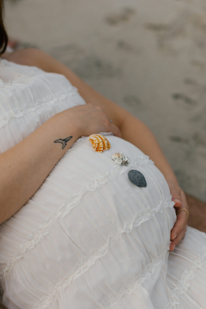 Close-up of mother’s hands resting on her pregnant belly with ocean light reflecting around her.