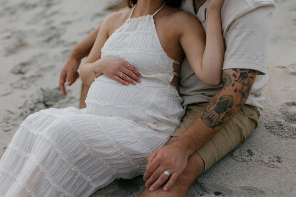 Intimate moment between couple seated on dunes, ocean breeze moving through tall grass.