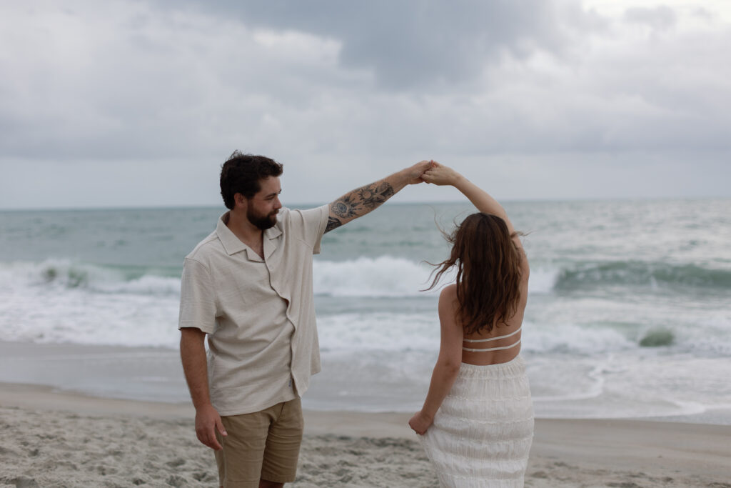 Couple walking hand in hand through wet sand, small waves washing over their footprints.