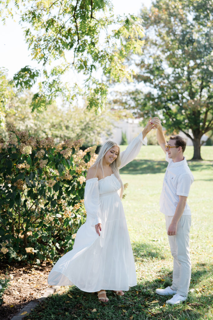 Bride posing in flowy white dress among hydrangea bushes during engagement photos