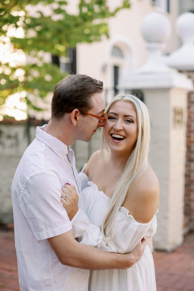 Groom whispering to bride while she laughs near white stone gate in Frederick Maryland