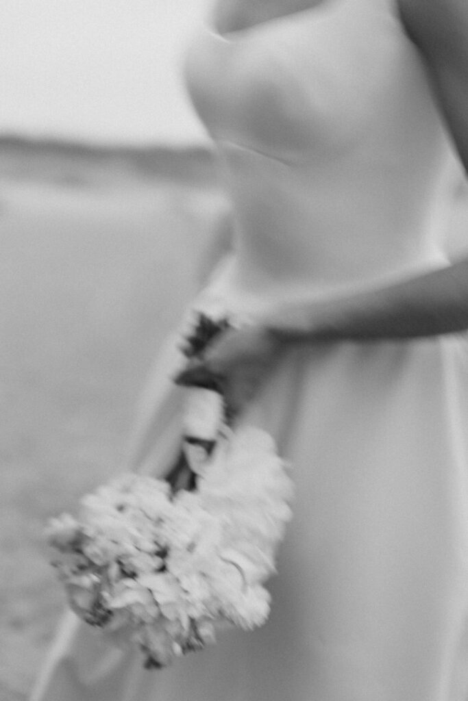 Fine-art blurred motion photo of bride holding bouquet on the beach in black and white.