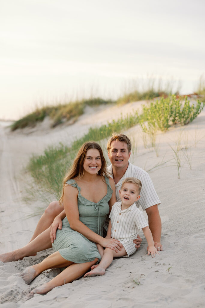 Family of three smiling together during a sunset beach portrait session in Atlantic Beach on North Carolina's Crystal Coast.