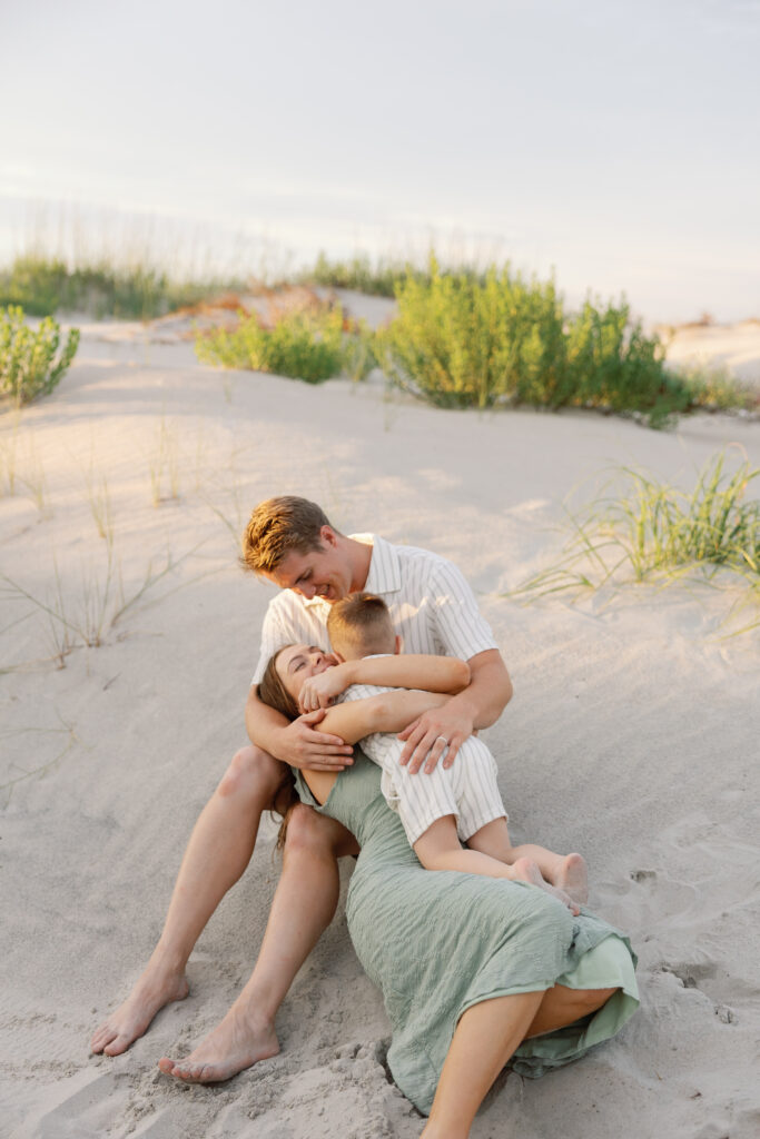 Family embracing on the sand dunes during a sunset portrait session with an Atlantic Beach NC family photographer.