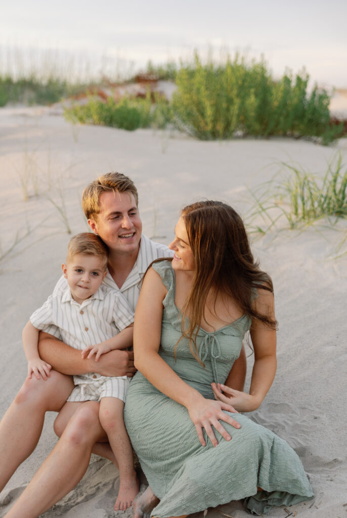 Smiling family sitting together on the sandy dunes during golden hour at Atlantic Beach, NC.