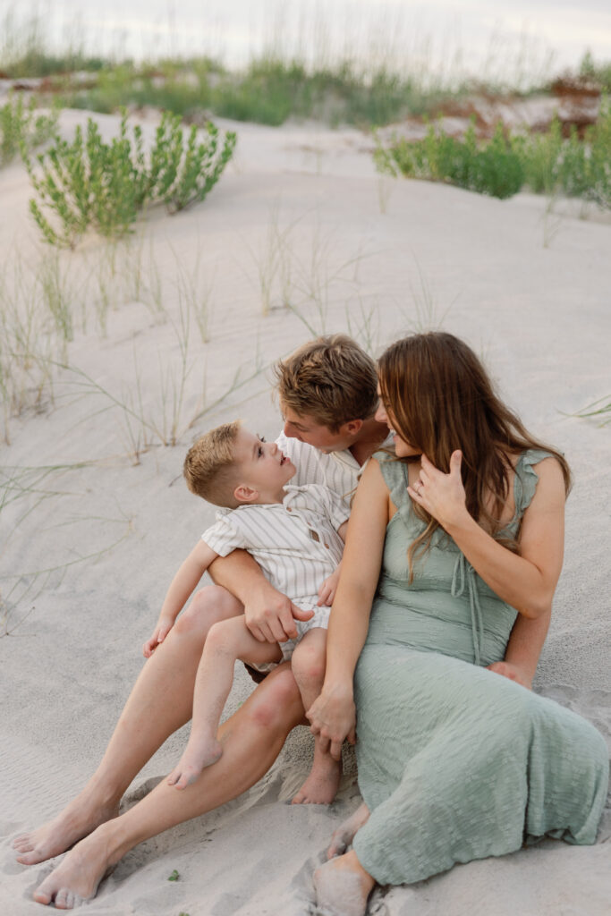 Parents sharing a joyful moment with their son during a relaxed sunset family session on Atlantic Beach, North Carolina.