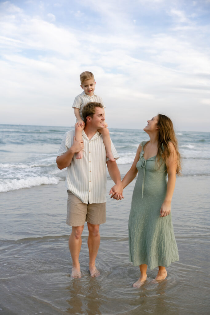 A family walks the shoreline of Atlantic Beach, North Carolina laughing and holding hands. 
