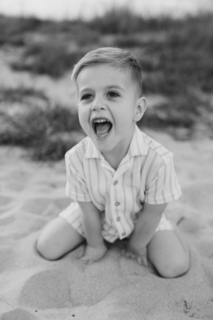 A child laughing in the sand during a family photo session on the Crystal Coast. 