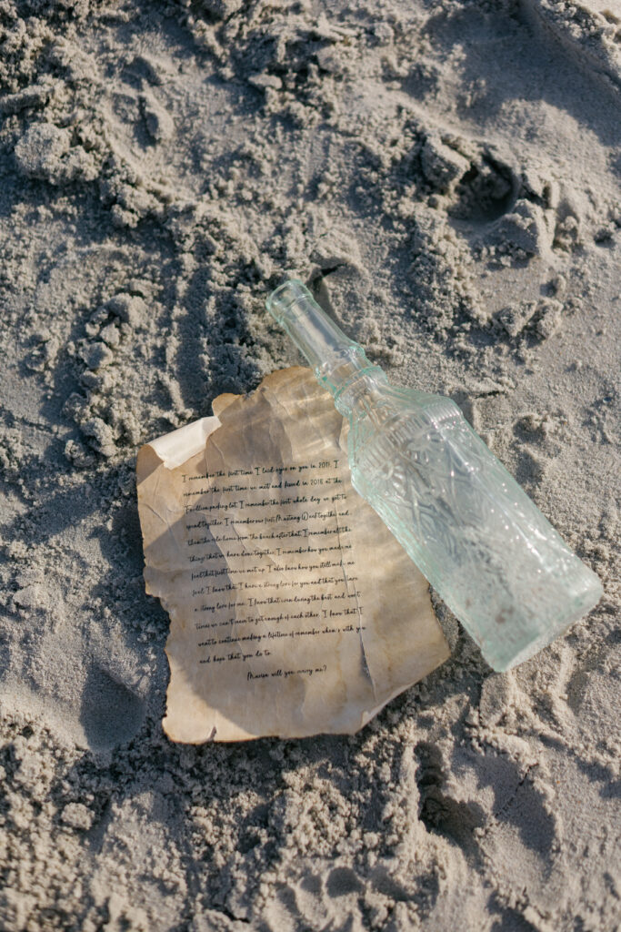 Creative beach proposal featuring a handwritten message in a bottle along the shoreline.
