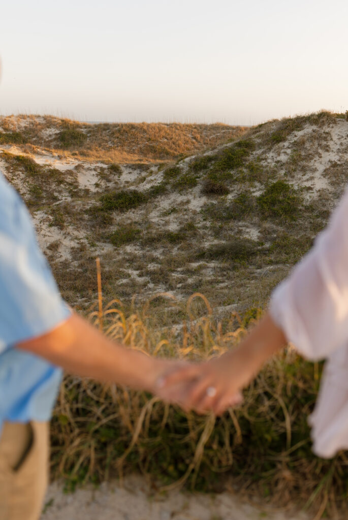 Newly engaged couple walking hand in hand along the beach during golden hour on North Carolina's Crystal Coast.