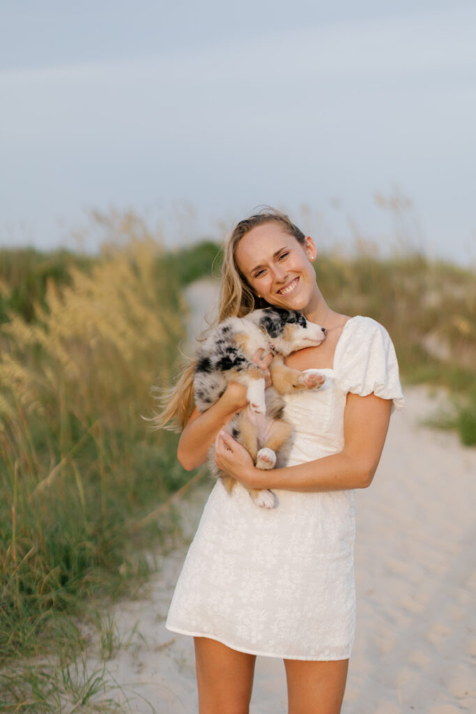Graduate holding her puppy among the sea oats during an Atlantic Beach NC senior portrait session